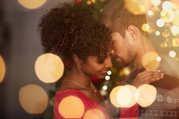 Loving couple embracing with warm lights Romantic couple in sweaters dancing before new year eve at home. Young lovely man and african woman hugging over christmas bokeh lights. Multiethnic couple dancing in love with golden lights bokeh in background. falling in love photos stock pictures, royalty-free photos & images