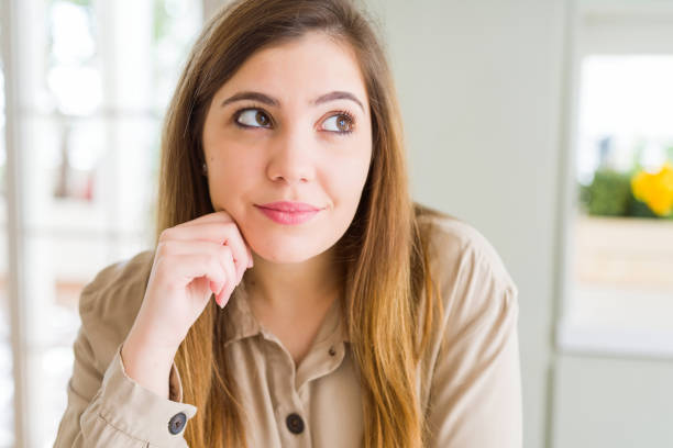 istock Beautiful young woman at home with hand on chin thinking about question, pensive expression. Smiling with thoughtful face. Doubt concept. 1158247159