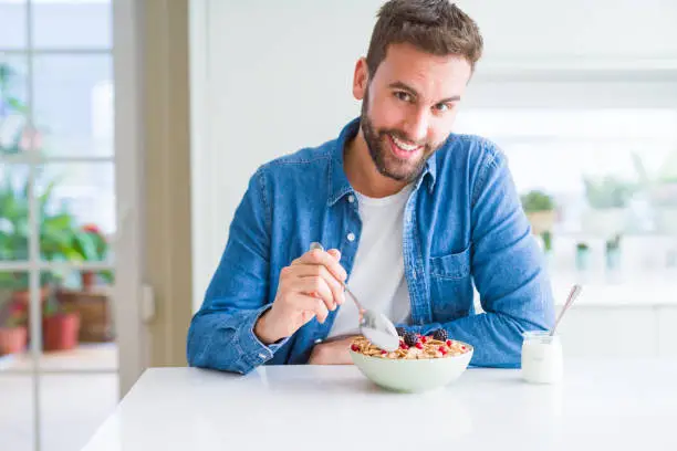 Photo of Handsome man having breakfast eating cereals at home and smiling