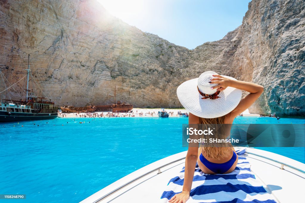 Woman on a boat enjoys the view to the shipwreck beach, Navagio in Zakynthos, Greece Beautiful, blonde woman in a bikini on a boat enjoys the view to the famous shipwreck beach, Navagio, in the island of Zakynthos, Greece Greece Stock Photo