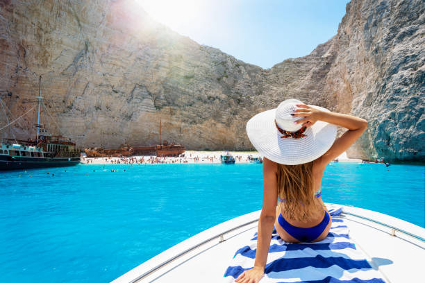 Woman on a boat enjoys the view to the shipwreck beach, Navagio in Zakynthos, Greece Beautiful, blonde woman in a bikini on a boat enjoys the view to the famous shipwreck beach, Navagio, in the island of Zakynthos, Greece yacht photos stock pictures, royalty-free photos & images