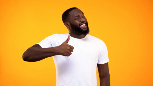 istock Young bearded black guy showing thumbs up, smiling on camera yellow background 1158248796