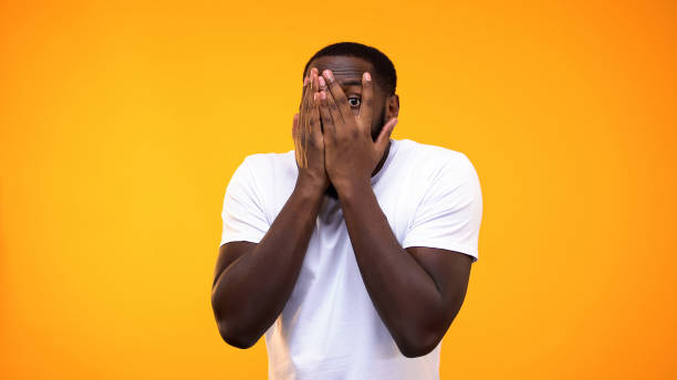 istock Surprised afro american guy peeping through fingers against yellow background 1158248804