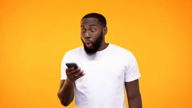 Photo of Surprised afro-american guy looking at phone screen, lottery winner, betting app