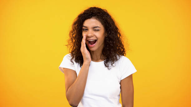 istock Smiling woman whispering secrets and winking on camera yellow background, rumors 1158248925
