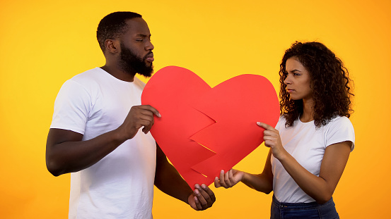 Offended boyfriend and girlfriend holding paper heart parts, relations conflict