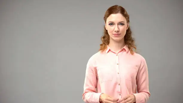 Red-haired woman in pink blouse looking in camera on grey background, template