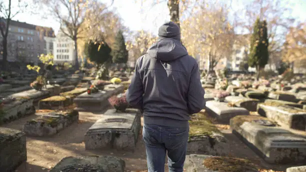 Sad man walking on ancient cemetery, visiting relative, commemorating ancestors