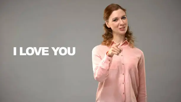 Young female saying love you in sign language, text on background, gesturing