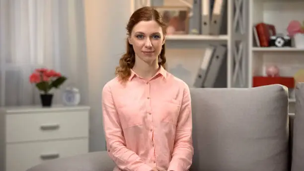 Young caucasian female looking in camera sitting on sofa, home comfort, rest