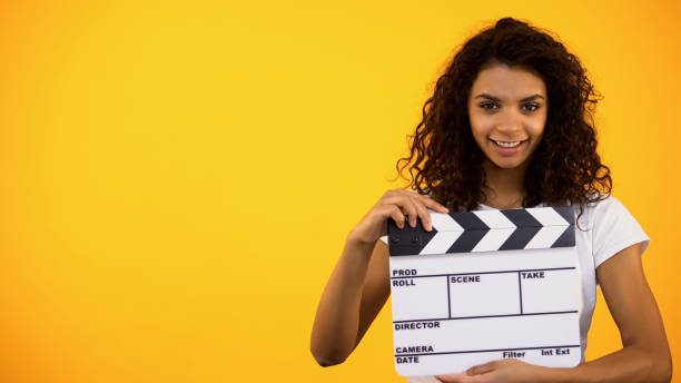 istock Smiling young female holding clapper board on orange background, cinematography 1158249956