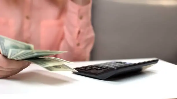 Woman dollars in hand counting taxes, calculator on table, financial investment