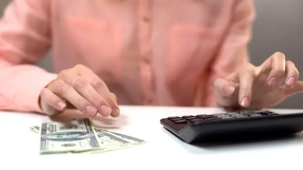 Female calculating monthly expenses, dollar banknotes on table, taxes payment