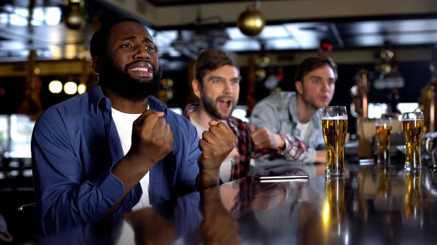 uomo afro-americano emotivi che fa il tifo per la squadra preferita con gli amici al bar - overemotional foto e immagini stock