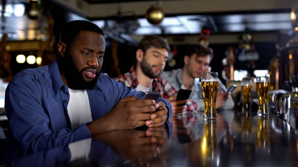 istock Sad multiethnic men surfing internet on phones in pub instead of communicating 1158250398