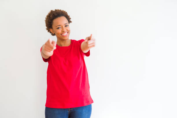 白い背景の上に若い美しいアフリカ系アメリカ人の女性指であなたとカメラを指し、肯定的で陽気な笑顔 - african descent casual clothing looking at camera ストックフォトと画像