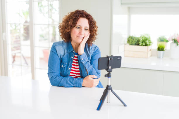 istock Senior woman doing video chat using smartphone camera thinking looking tired and bored with depression problems with crossed arms. 1158253264