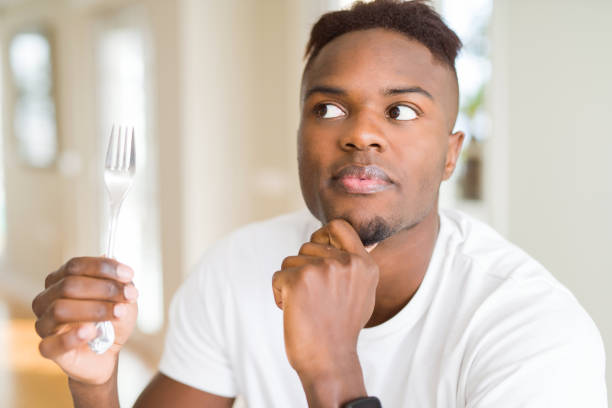 istock African american man holding silver fork cutlery serious face thinking about question, very confused idea 1158254118