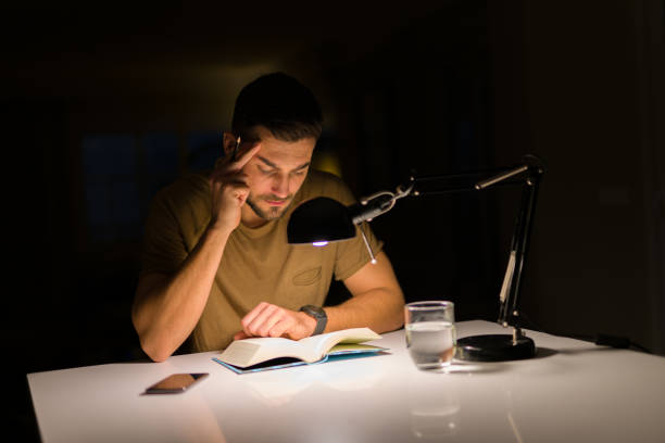 istock Young handsome man studying at home, reading a book at night 1158256710