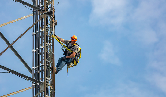Canton, Ohio lake, USA. May 8, 2019. Communication maintenance. Technician climbing on telecom tower antenna against blue sky background, copy space