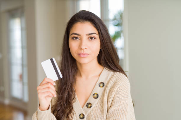 istock Young woman holding credit card as payment with a confident expression on smart face thinking serious 1158258506