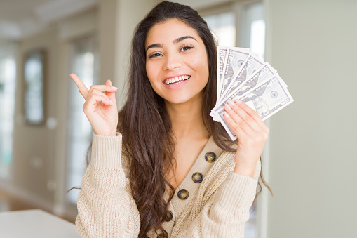 Young woman holding 50 dollars bank notes very happy pointing with hand and finger to the side