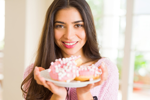 Beautiful young woman smiling holding a plate full of delicious pink donuts