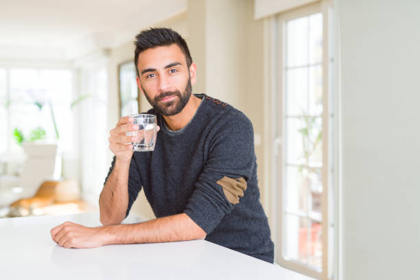 istock Handsome hispanic man drinking a fresh glass of water with a confident expression on smart face thinking serious 1158259496