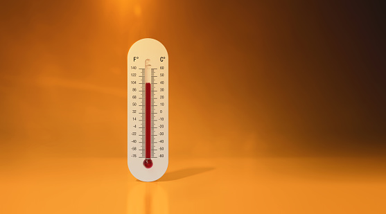 Extreme heat wave and high temperature concept. Thermometer standing on a reflective surface under a hot sun sky. Horizontal composition with copy space.