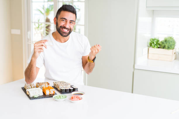 istock Handsome hispanic man eating asian sushi using chopsticks screaming proud and celebrating victory and success very excited, cheering emotion 1158260023