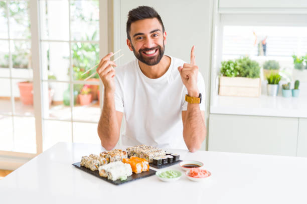 Handsome hispanic man eating asian sushi using chopsticks surprised with an idea or question pointing finger with happy face, number one