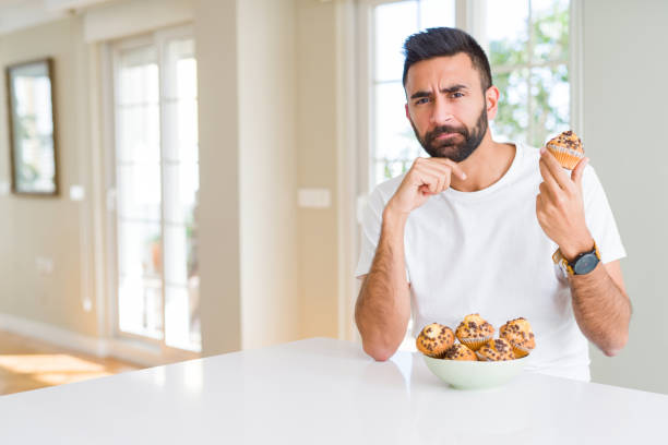 istock Handsome hispanic man eating chocolate chips muffin serious face thinking about question, very confused idea 1158260061