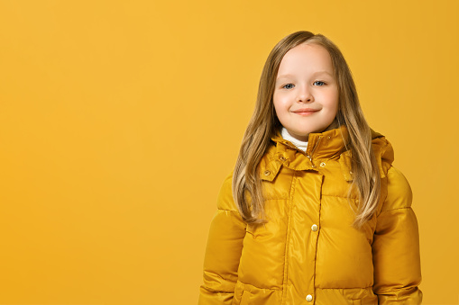 Portrait of a cheerful little girl in jacket over yellow background. Autumn concept. Copy space