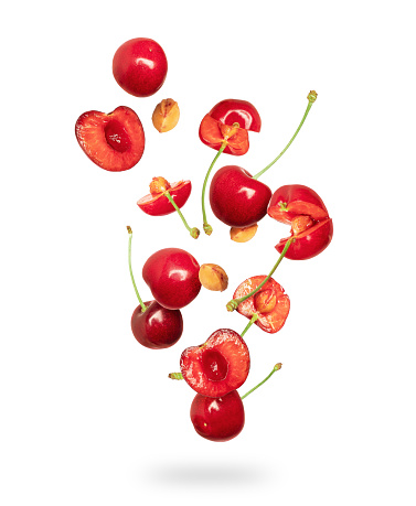 Whole and sliced fresh cherries in the air on a white background