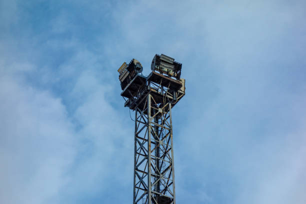 Old huge industrial spot light lamp system on blue sky background. Aged metal tower frame construction with powerful halogen and bulb lamps to illuminate stadium or big technology and transport object