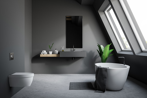 Gray attic bathroom interior with concrete floor, bathtub with rug near it, sink with narrow mirror and toilet. 3d rendering