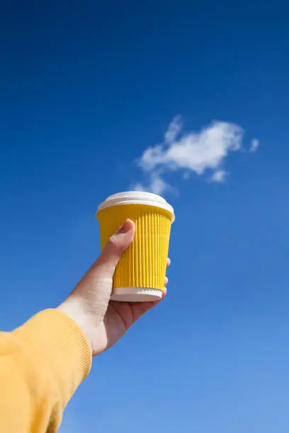 Close-up of female hand holding hot craft cup of coffee at early morning against the blue sky. Enjoy, lifestyle, take away breakfast concept.