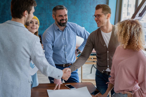 istock Glad to work with you! Young modern men in smart casual wear shaking hands and smiling while working in the creative office. 1158281400