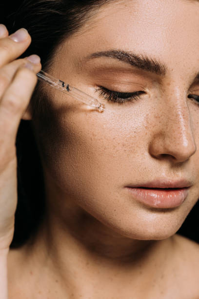 jeune femme attirante appliquant le sérum sur le visage avec la pipette - tache de rousseur photos et images de collection