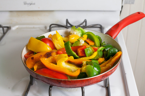 Sliced green, orange, red, and yellow bell peppers and poblano peppers in a frying pan