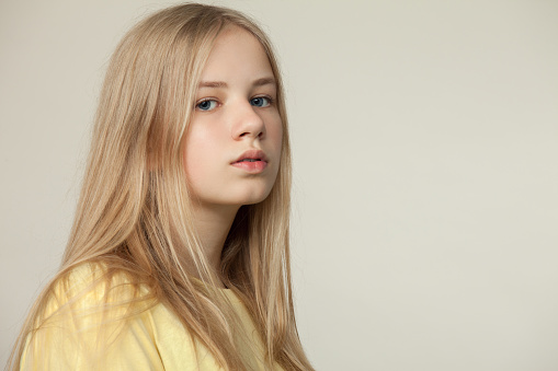 Studio portrait of a blonde teen girl in a yellow t-shirt on a beige background