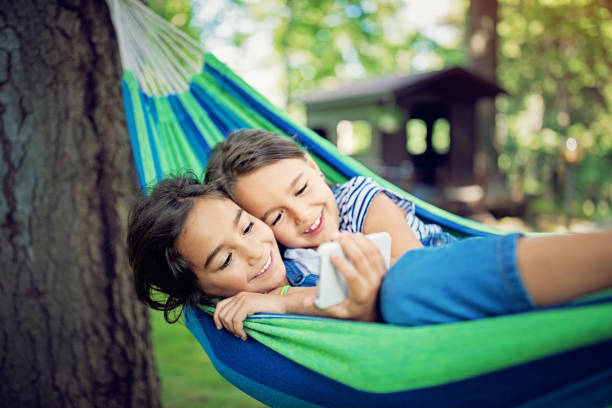 istock Sisters are lying down in the hammock and looking in a mobile phone 1158302809