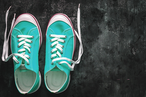 blue-cyan-green-turquoise sneakers with untied laces on a dark concrete background. Copy space. View from above