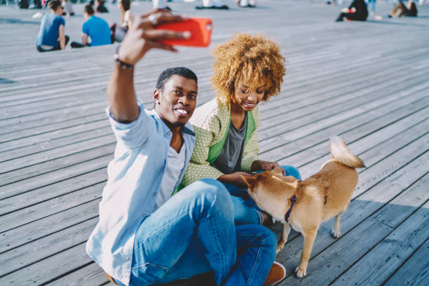 istock African american young man making selfie photo on modern smartphone while resting together with lovely girlfriend and dog in urban setting.Happy couple in love taking picture on front camera of phone 1158305055