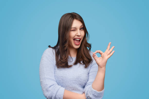 Cheerful woman winking and gesturing OK