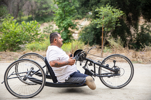 A mature hispanic man rides his handcycle. He is a double amputee.