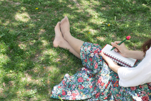 istock Woman sitting on the grass with cherry tree petals and red note 1158313421