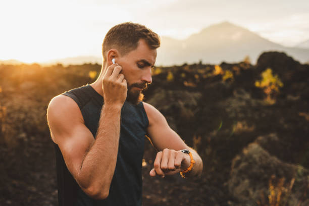 corredor masculino sincronizando auriculares inalámbricos con reloj inteligente. preparación para correr al aire libre al amanecer. - sun watch fotografías e imágenes de stock