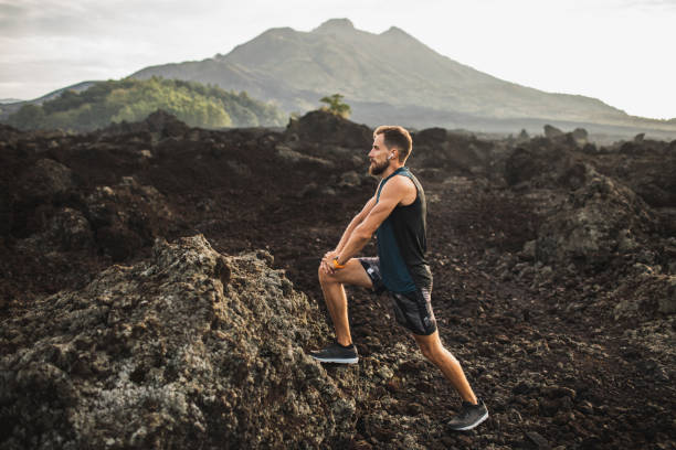 istock Young hipster runner with beard stretching and warming-up for trail running outdoors. Listening music in air pods. Mountain view on background. 1158317152