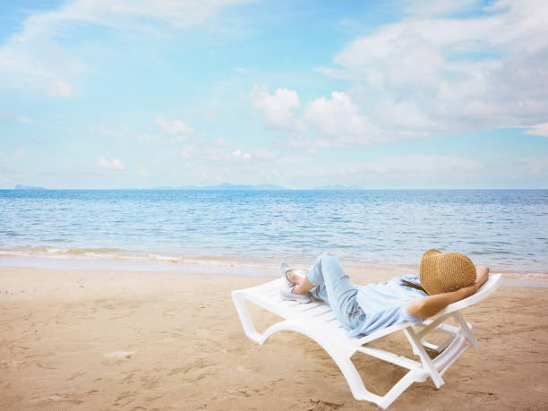 istock woman with hat relaxing on chair at beach 1158320054